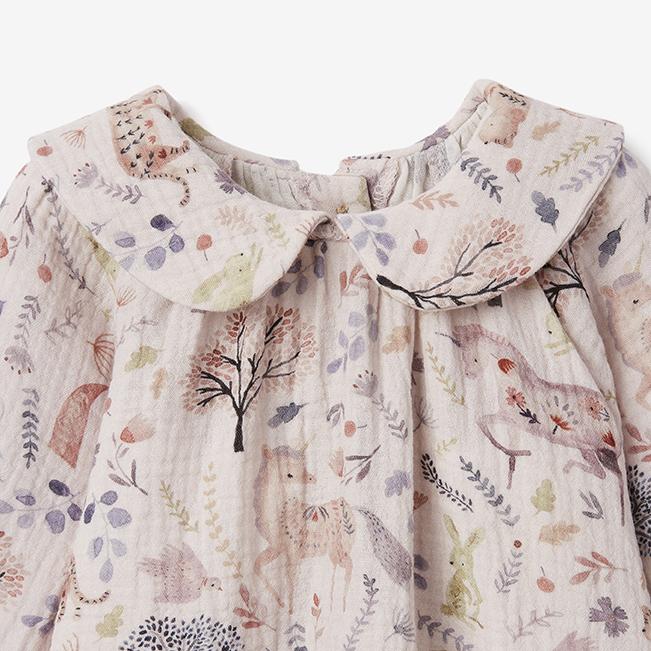 Close-up of organic cotton muslin unicorn baby dress with ruffled collar and botanical print on white background