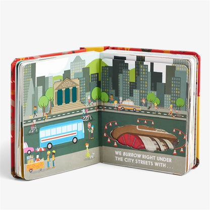 An open children's pop-up book showing a city street scene with buildings, a bus, pedestrians, and a tunnel entrance. The right page has the text, 'WE BURROW RIGHT UNDER THE CITY STREETS WITH.