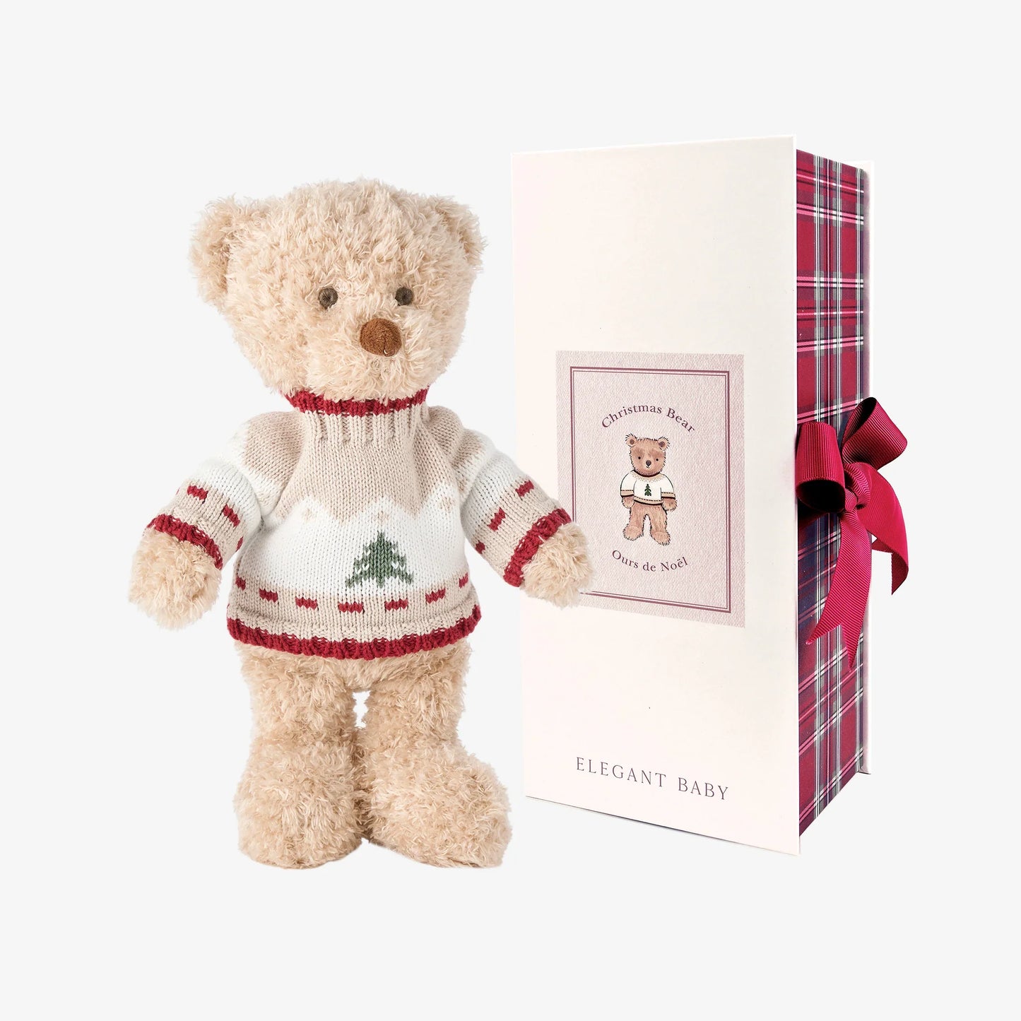 A plush teddy bear wearing a cream knit Christmas sweater with red trim and a green tree motif, standing beside its white gift box with red plaid wrapping and a pink ribbon. The box shows the brand name ELEGANT BABY.