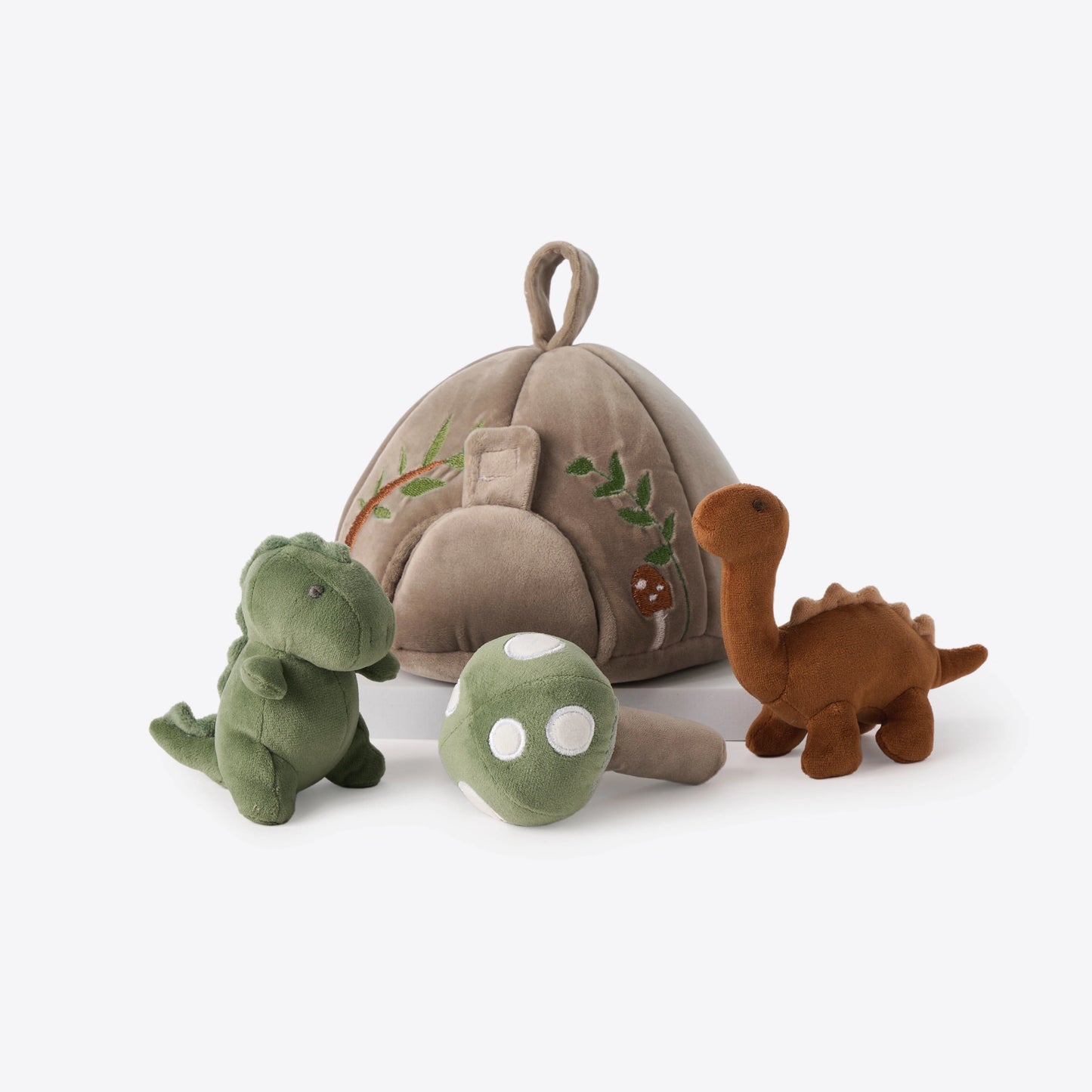 A plush dinosaur toy set on a clean white background, featuring a beige fabric dinosaur nest with embroidered details, a green T-Rex, a brown Brachiosaurus, and a green mushroom toy.