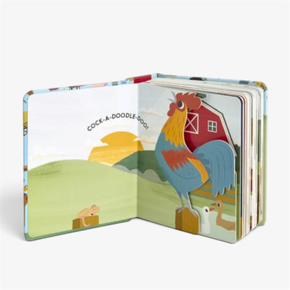 An open children's pop-up book showing a colorful illustration of a rooster in a farm scene with a barn, hills, and the text 'COCK-A-DOODLE-BOO!', photographed on a white background.
