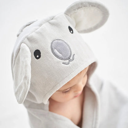 A baby wrapped in a light gray hooded towel or wrap, wearing a matching animal-ear hood with embroidered black eyes and a gray snout on a white background.