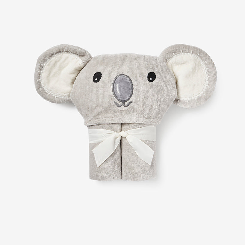 A light gray plush koala hooded towel with cream-colored inner ears and a cream ribbon bow at the bottom, shown against a plain light gray background.