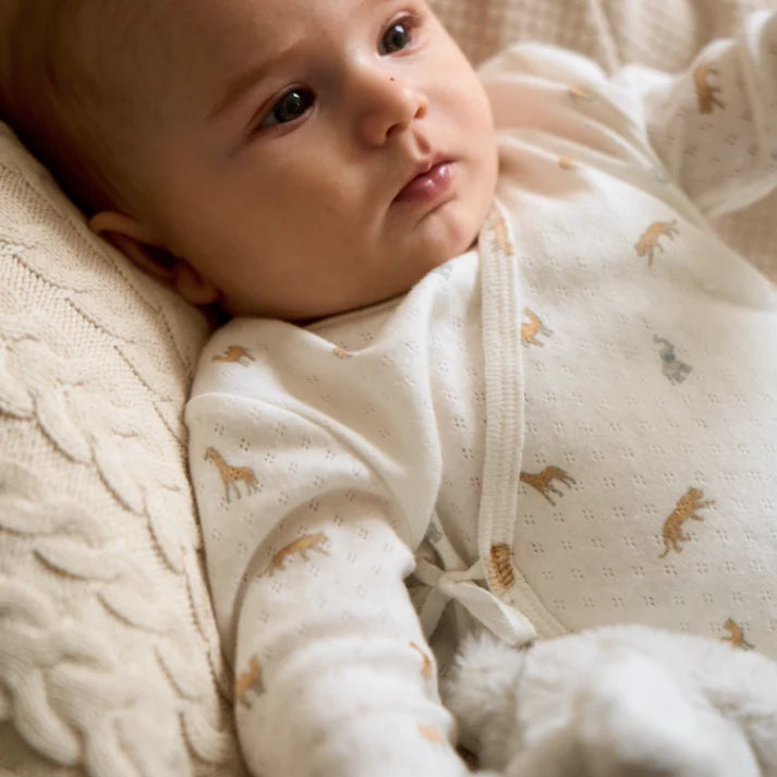 Baby in a white outfit with animal patterns lying on a soft surface