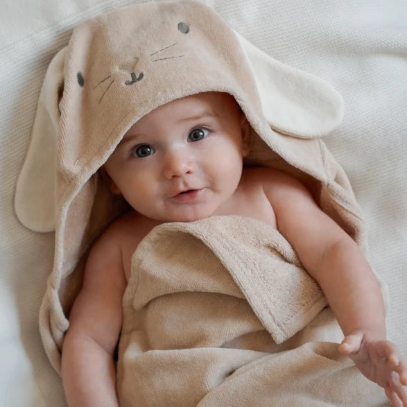 Baby wrapped in a beige towel with bunny ears on a soft surface