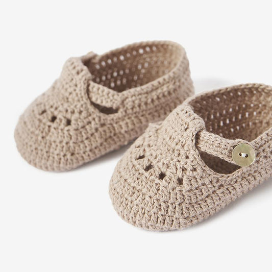 Close-up of doeskin beige knit baby booties with T-strap details on white background