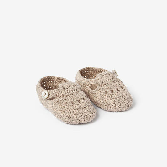 A pair of beige hand-crocheted baby booties with a t-strap style on white background