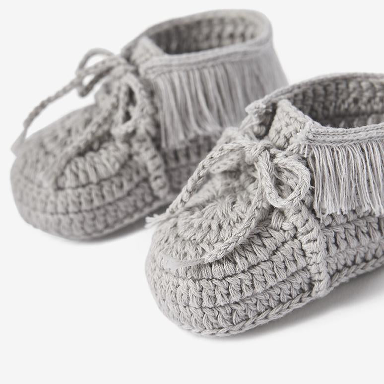 Close-up of gray knit moccasin baby booties with crochet texture and tie details on white background