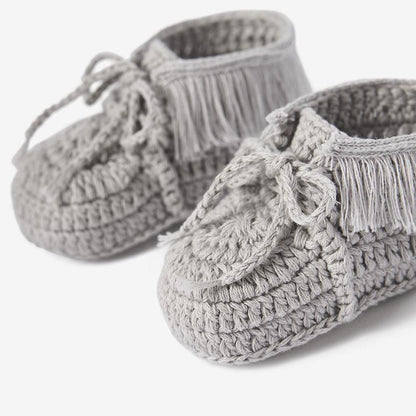 Close-up of gray knit moccasin baby booties with crochet texture and tie details on white background