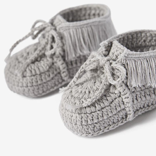 Close-up of gray knit moccasin baby booties with crochet texture and tie details on white background