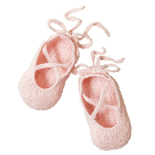 Pair of pink hand-crocheted cotton ballerina baby booties with ankle ties on white background