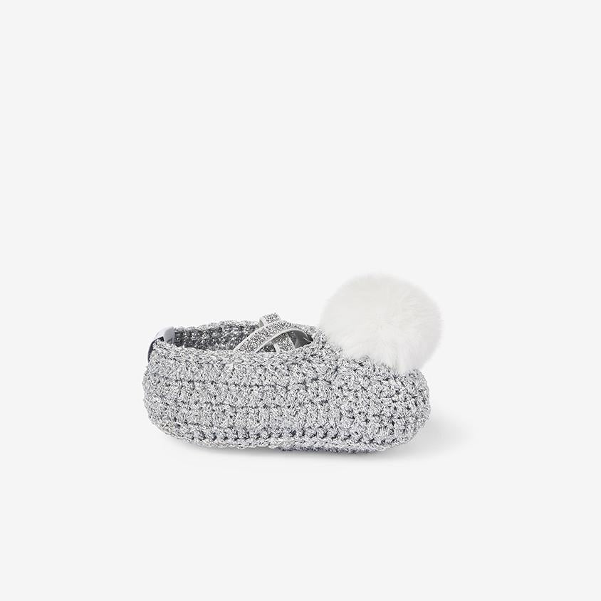 Side view of silver metallic hand-crocheted baby booties with pom-pom detail on white background