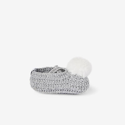 Side view of silver metallic hand-crocheted baby booties with pom-pom detail on white background